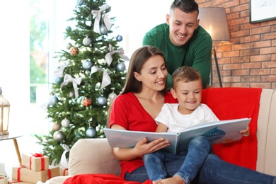 Happy parents and child reading fairy tales together at home on Christmas day