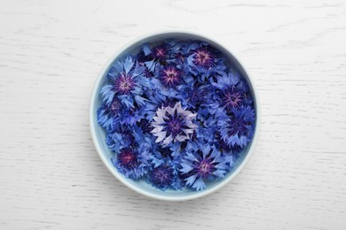 Photo of Beautiful colorful cornflowers in bowl on white wooden table, top view