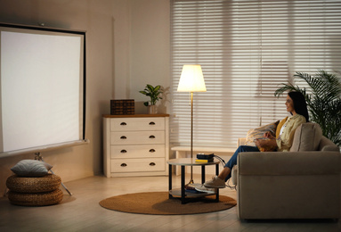 Photo of Young woman watching movie using video projector at home