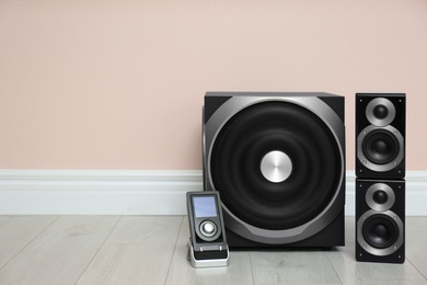 Photo of Modern powerful audio speaker system on floor near pink wall. Space for text