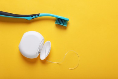 Photo of Container with dental floss and toothbrush on yellow background, top view. Space for text