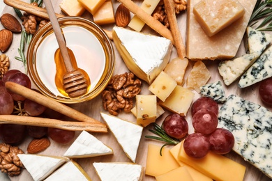 Photo of Cheese plate with honey, grapes and nuts on wooden board, top view