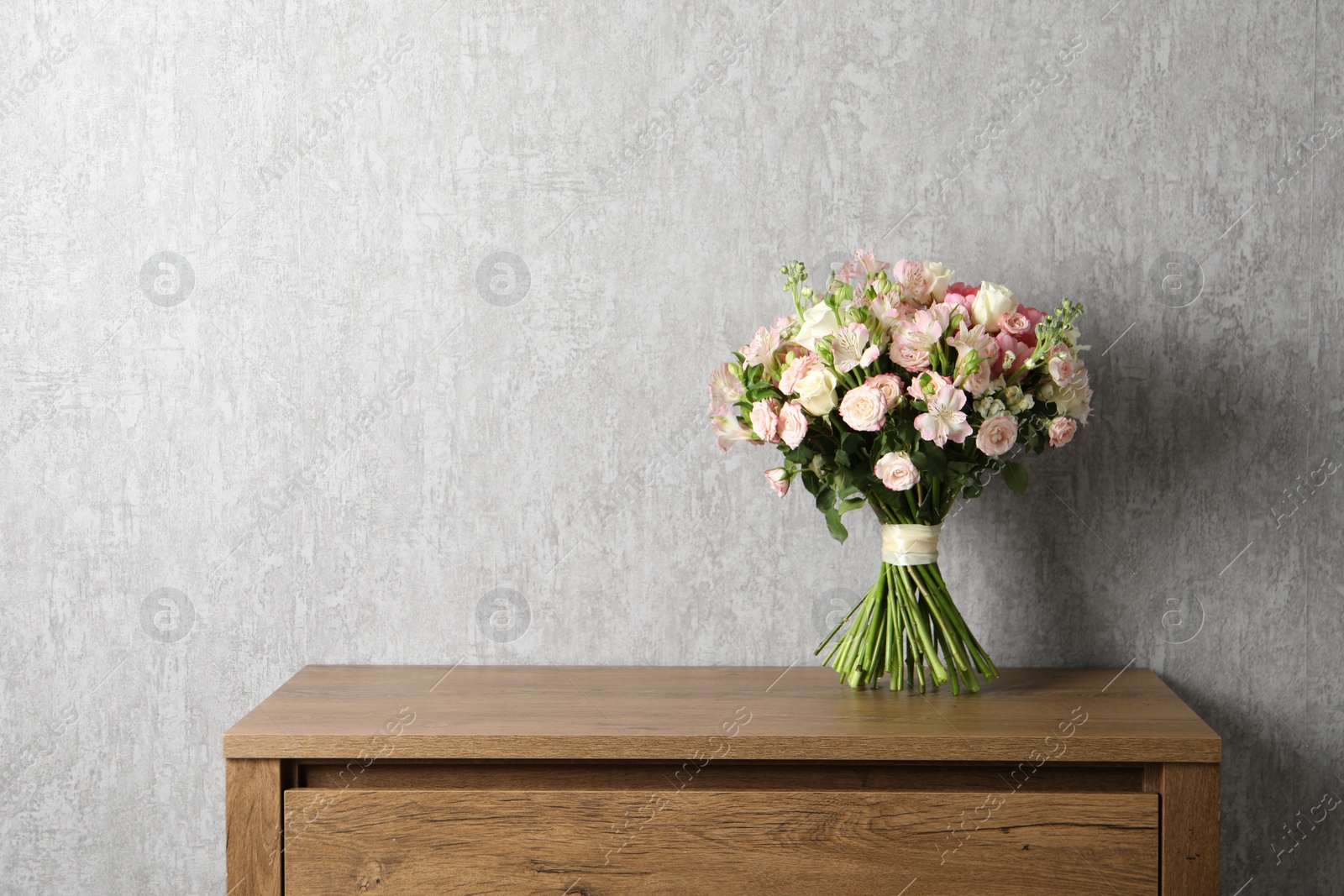 Photo of Beautiful bouquet of fresh flowers on wooden table near grey wall, space for text