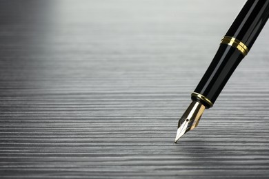 Photo of Stylish fountain pen on black wooden table, closeup. Space for text
