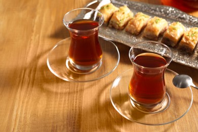 Photo of Traditional Turkish tea in glasses and fresh baklava on wooden table