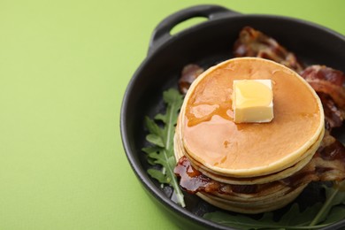 Tasty pancakes with butter, fried bacon and fresh arugula on light green background. Space for text