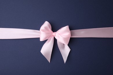 Photo of Pink satin ribbon with bow on blue background, top view