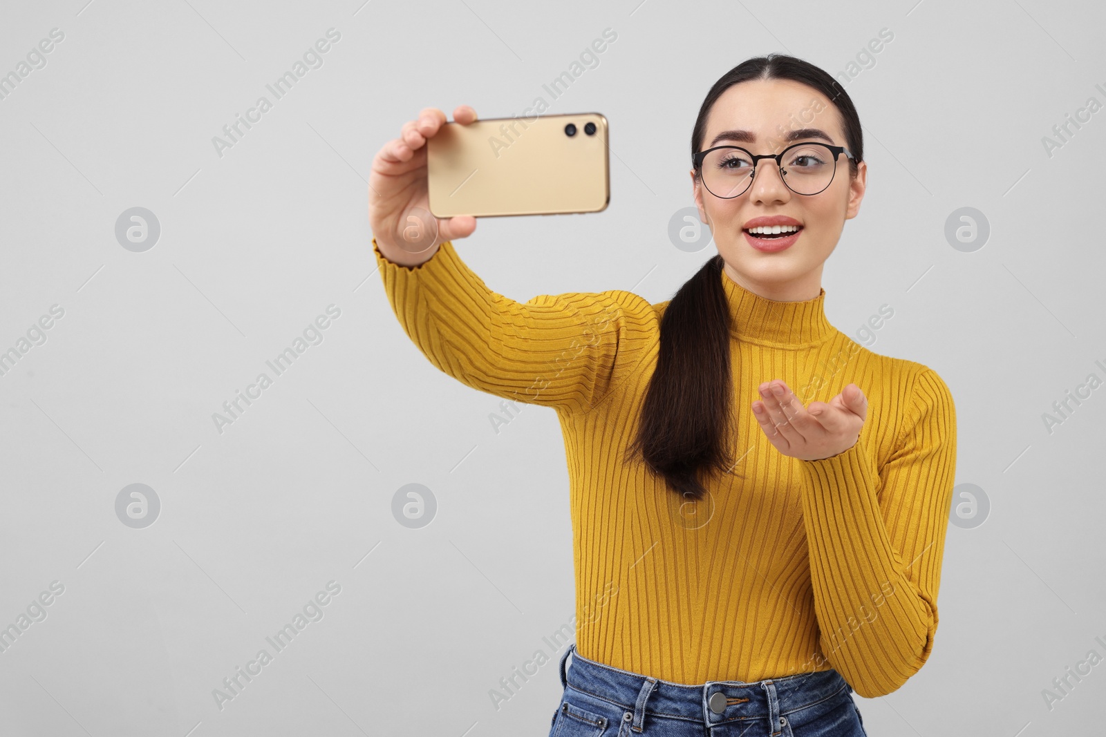 Photo of Smiling young woman taking selfie with smartphone on grey background, space for text
