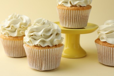 Photo of Tasty vanilla cupcakes with cream on pale yellow background, closeup