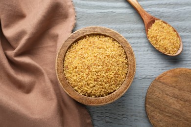 Photo of Bowl and spoon with uncooked bulgur on grey wooden table, flat lay