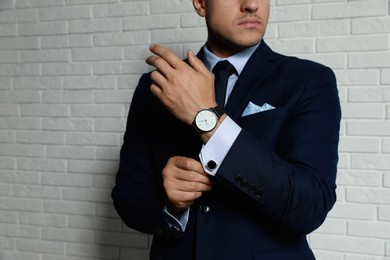 Photo of Stylish man putting on cufflink near white brick wall, closeup