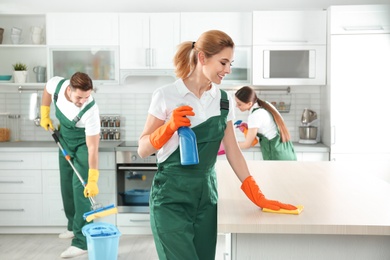 Photo of Woman using rag and sprayer for cleaning table with colleagues in kitchen