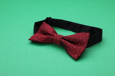 Stylish burgundy bow tie with polka dot pattern on green background