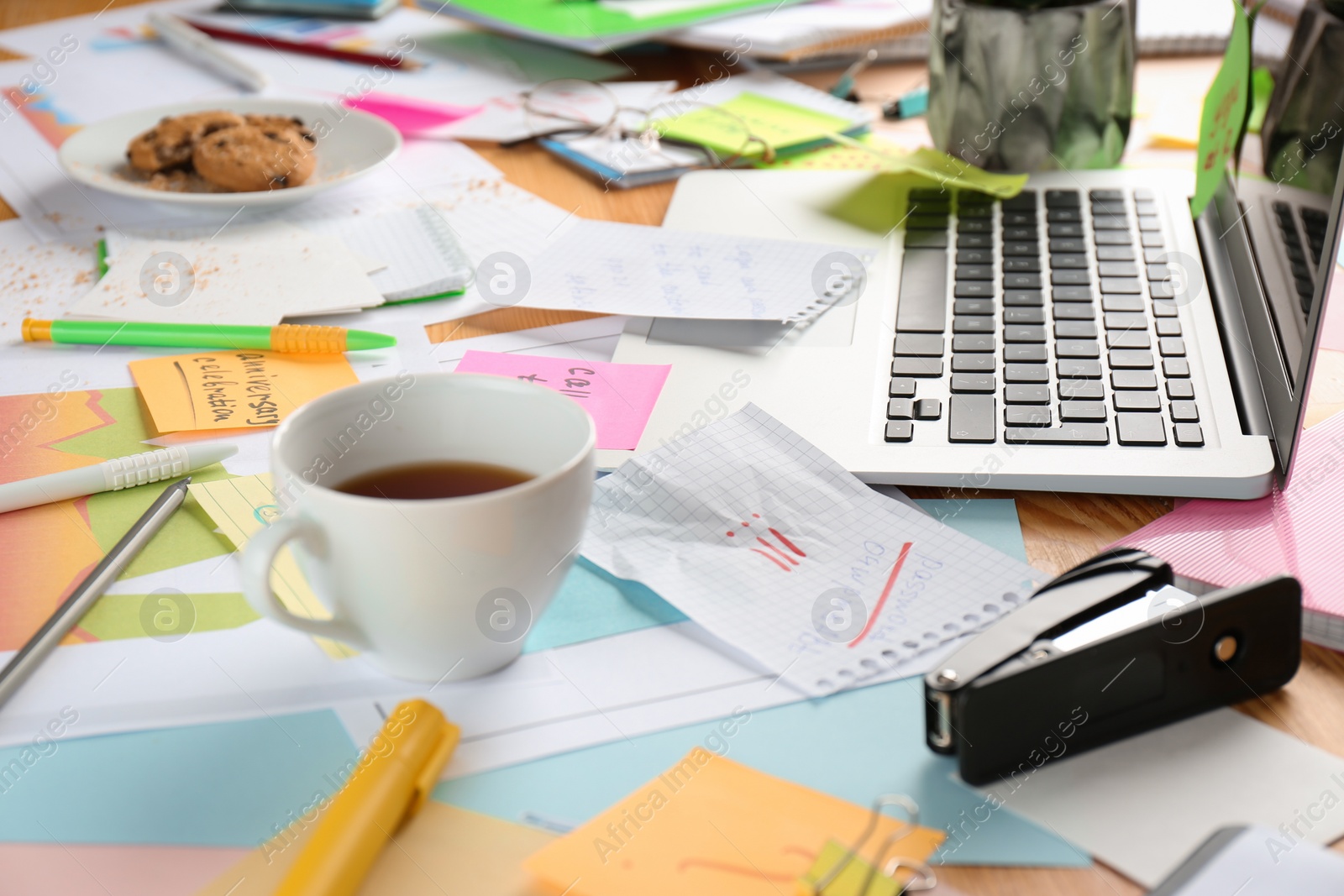 Photo of Messy table with laptop and tea. Concept of being overwhelmed by work