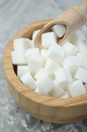 White sugar cubes in wooden bowl and scoop on grey table, closeup