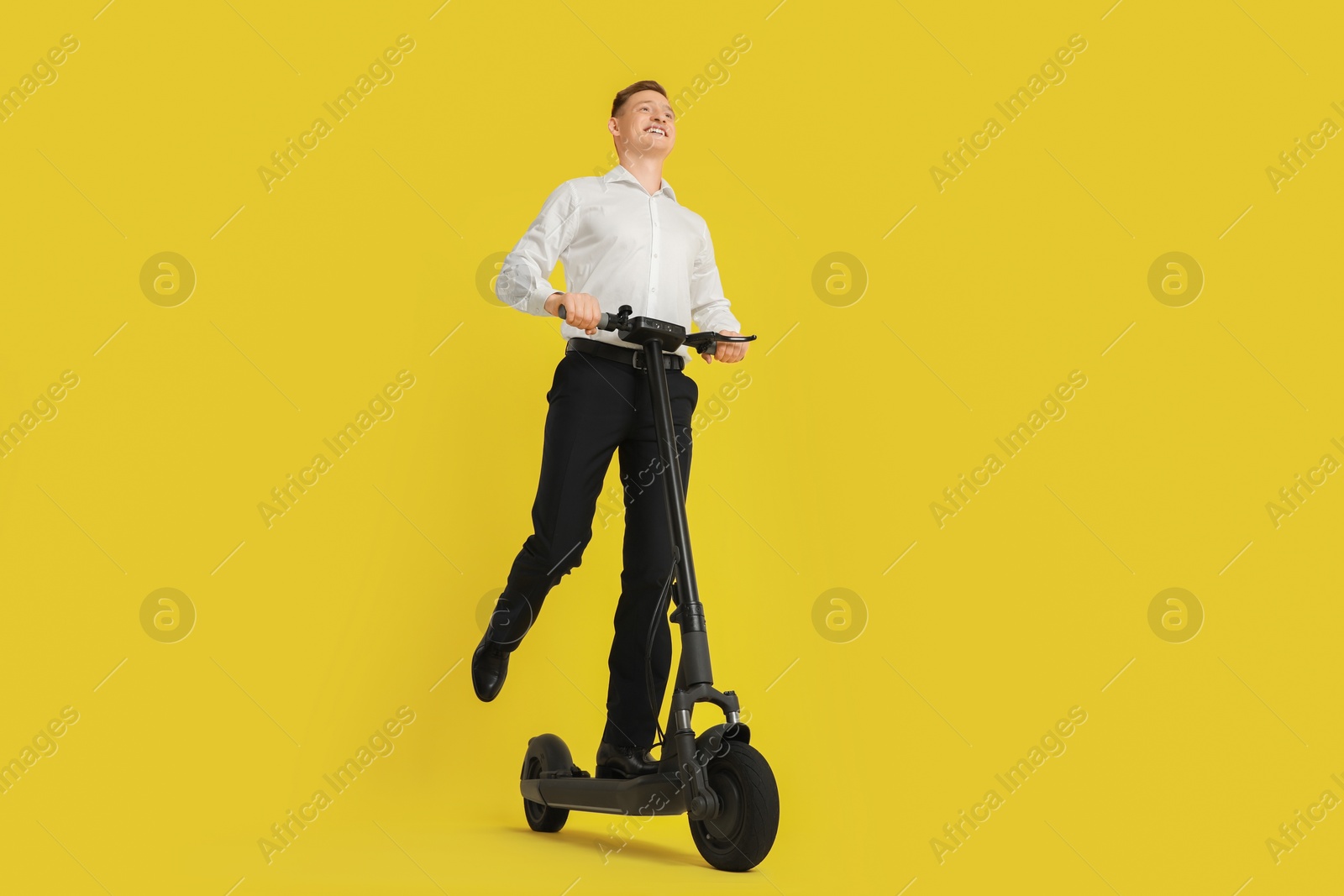 Photo of Happy man riding modern electric kick scooter on yellow background, low angle view