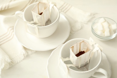 Photo of Cups with drip coffee bags on white table, closeup