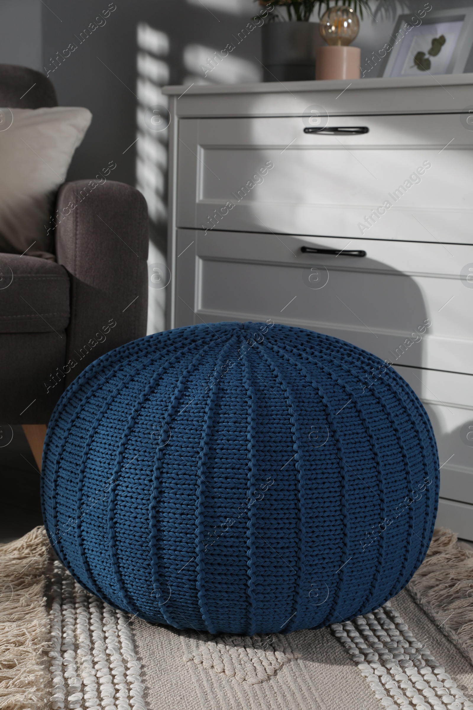 Photo of Stylish knitted pouf and chest of drawers in room. Home design