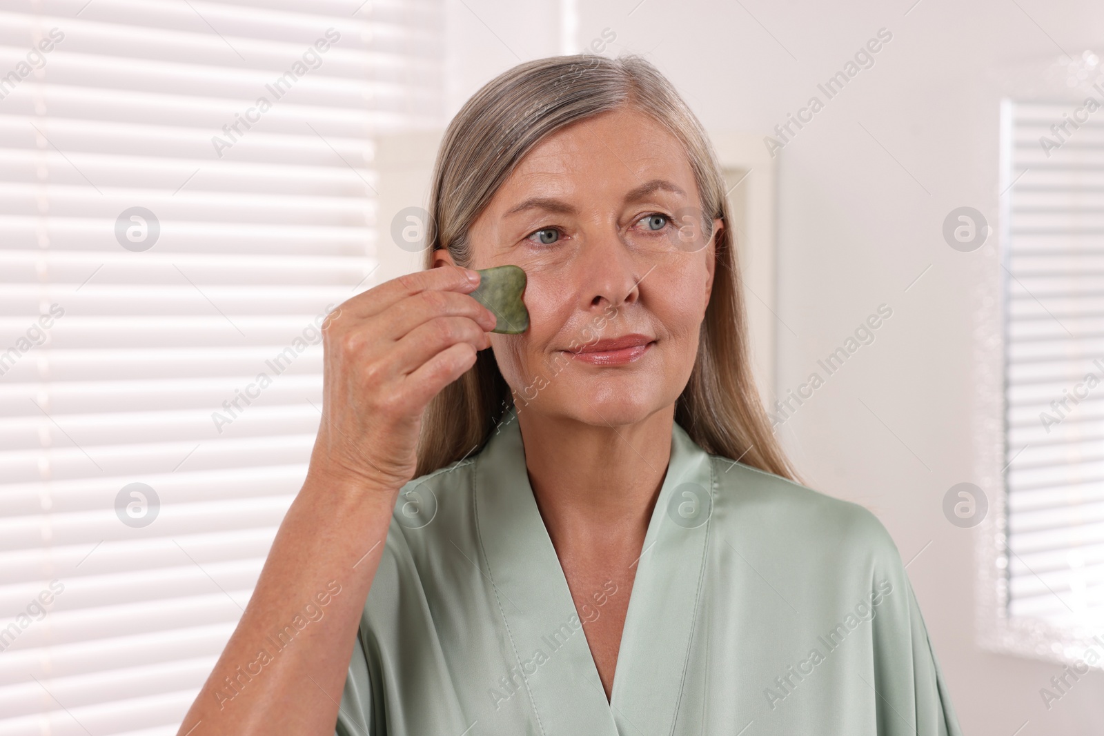 Photo of Woman massaging her face with jade gua sha tool in bathroom