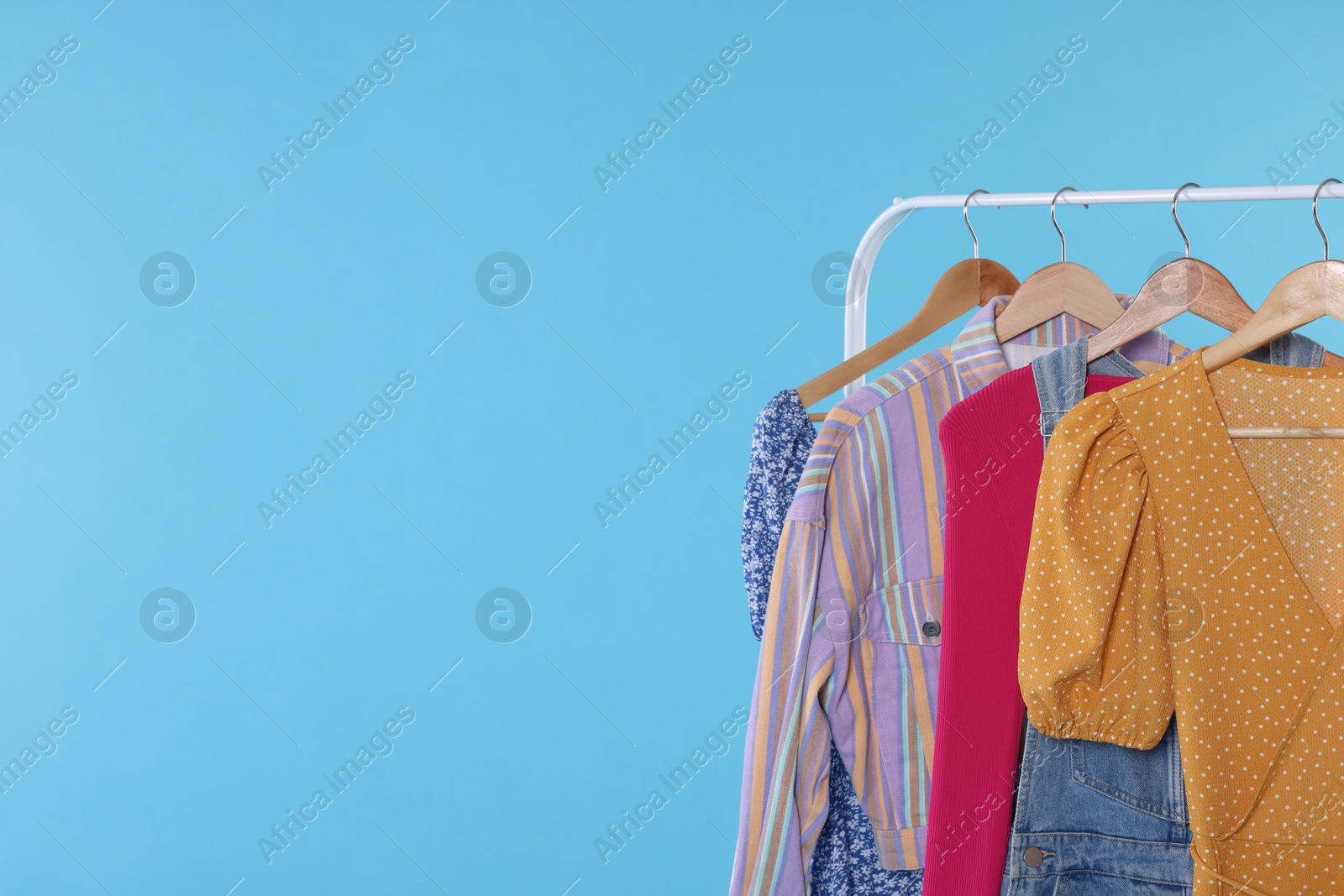 Photo of Rack with stylish women`s clothes on wooden hangers against light blue background, space for text