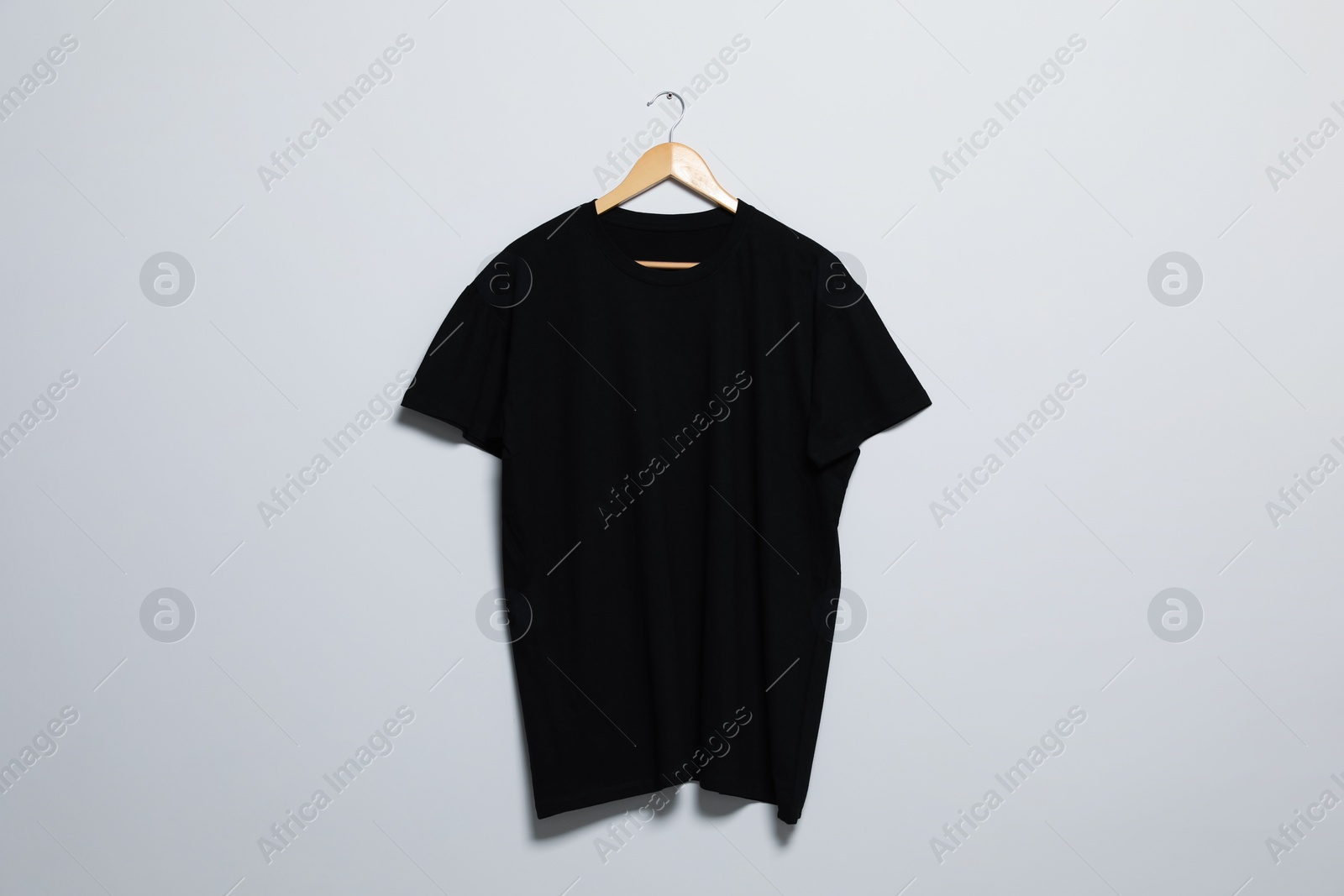 Photo of Hanger with black t-shirt on light wall. Mockup for design