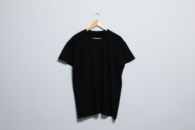 Photo of Hanger with black t-shirt on light wall. Mockup for design