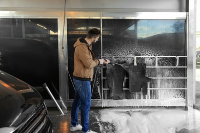 Photo of Man cleaning auto mats with high pressure water jet at self-service car wash
