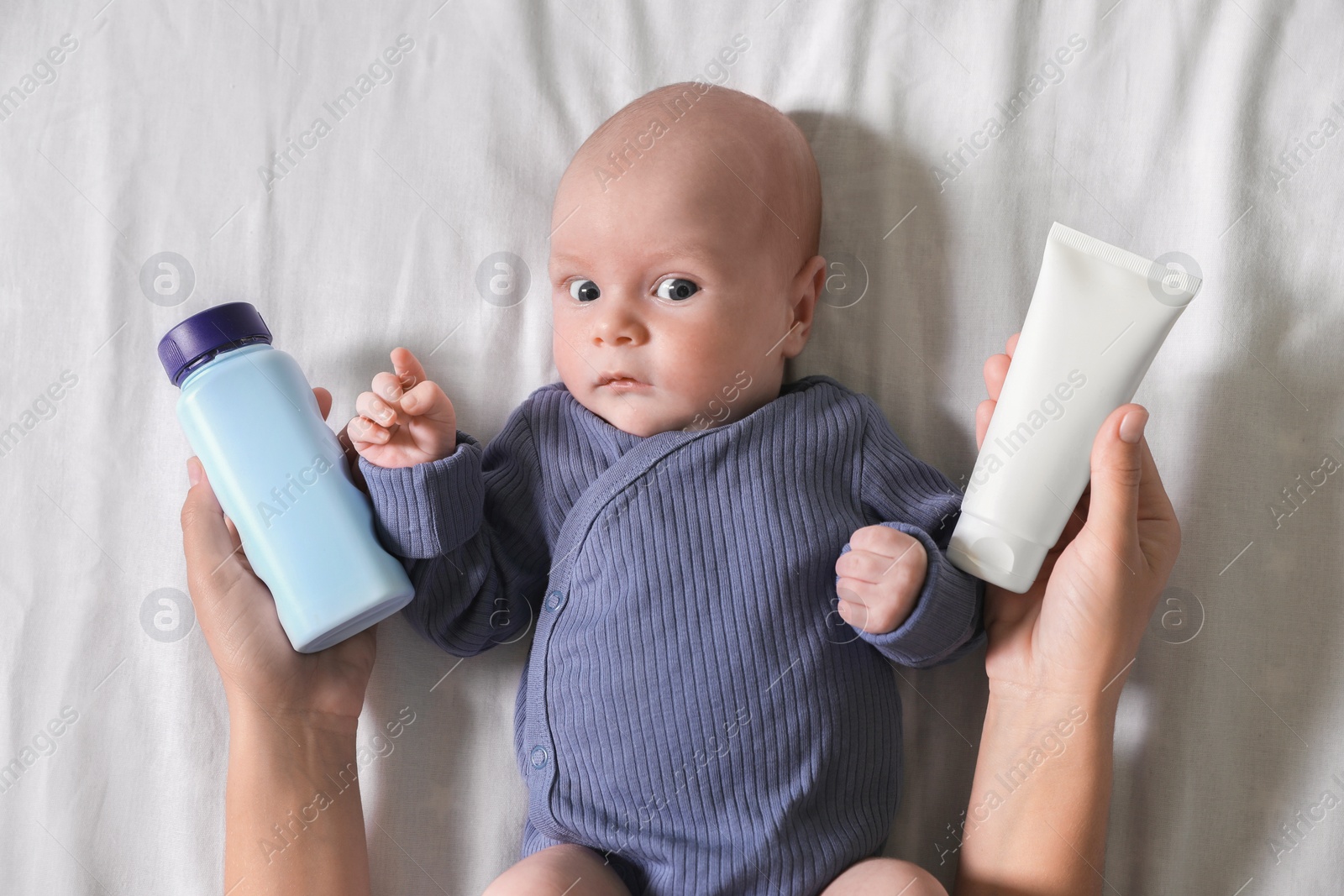 Photo of Mother holding body cream and dusting powder near cute little baby on bed, top view