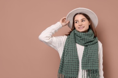 Photo of Beautiful woman in warm scarf and hat on brown background, space for text
