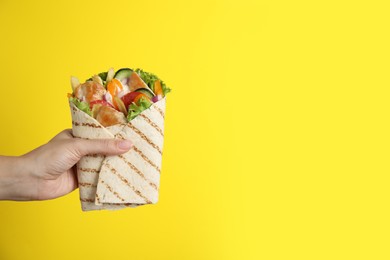 Photo of Woman holding delicious chicken shawarma on yellow background, closeup. Space for text