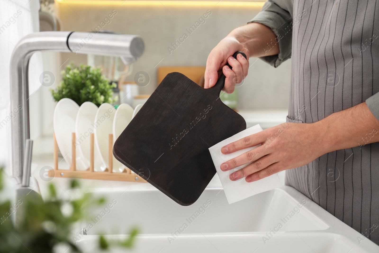 Photo of Man wiping dark wooden cutting board with paper napkin at sink in kitchen, closeup