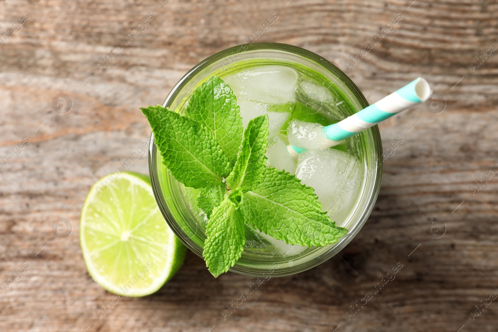 Photo of Refreshing beverage with mint and lime in glass on wooden background, top view