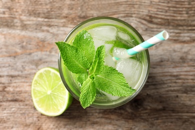 Refreshing beverage with mint and lime in glass on wooden background, top view