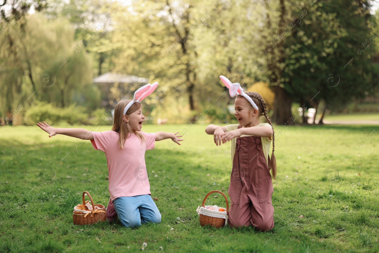 Photo of Easter celebration. Cute little girls in bunny ears with wicker baskets outdoors