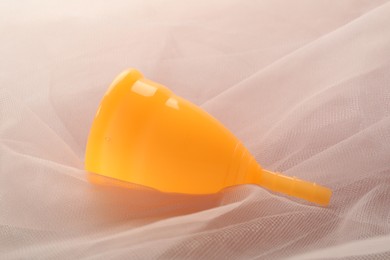 Photo of Orange menstrual cup on pink fabric, closeup
