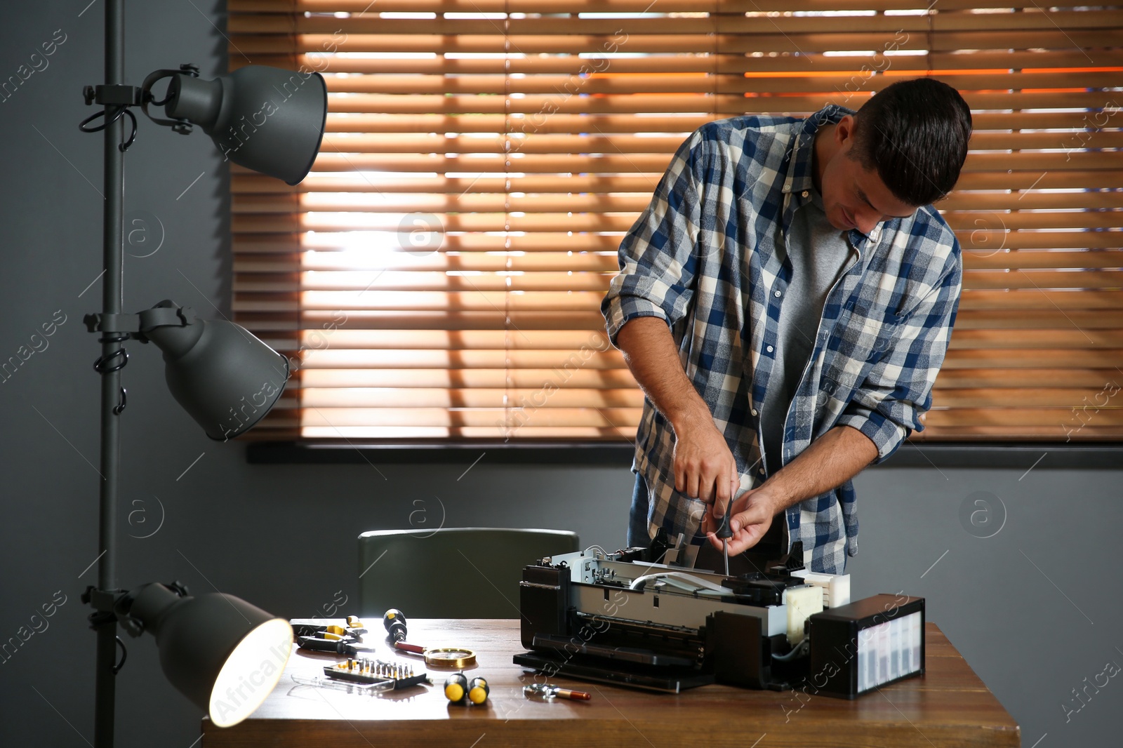 Photo of Repairman with screwdriver fixing modern printer in office