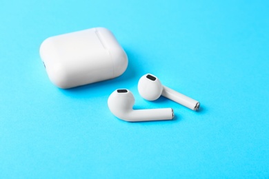 Photo of Modern wireless earphones and charging case on light blue background