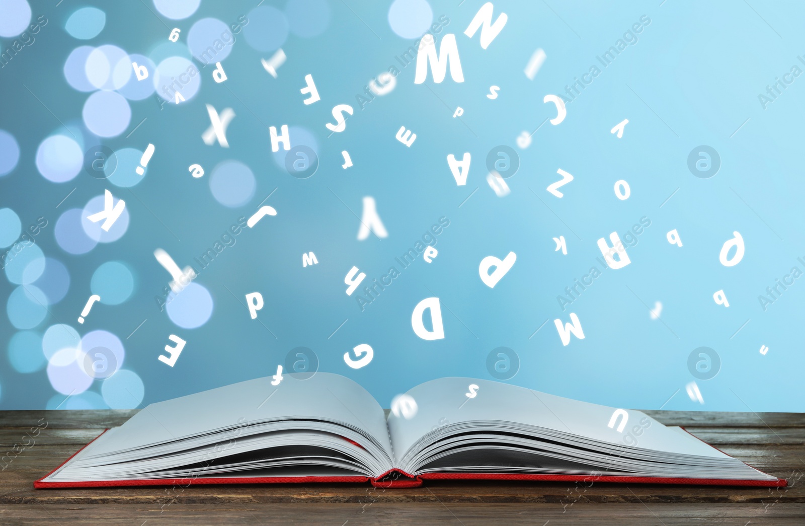 Image of Letters flying out from open book on wooden table, bokeh effect