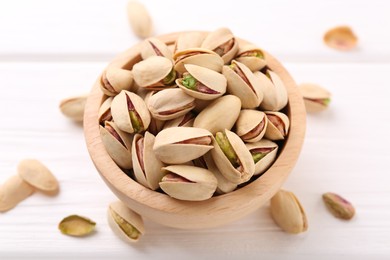 Tasty pistachios in bowl on white wooden table, closeup