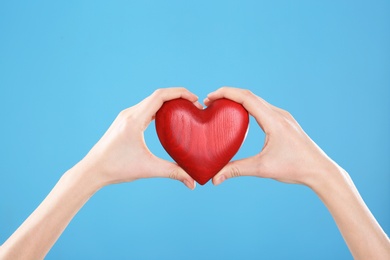 Photo of Woman holding decorative heart in hands on color background, closeup