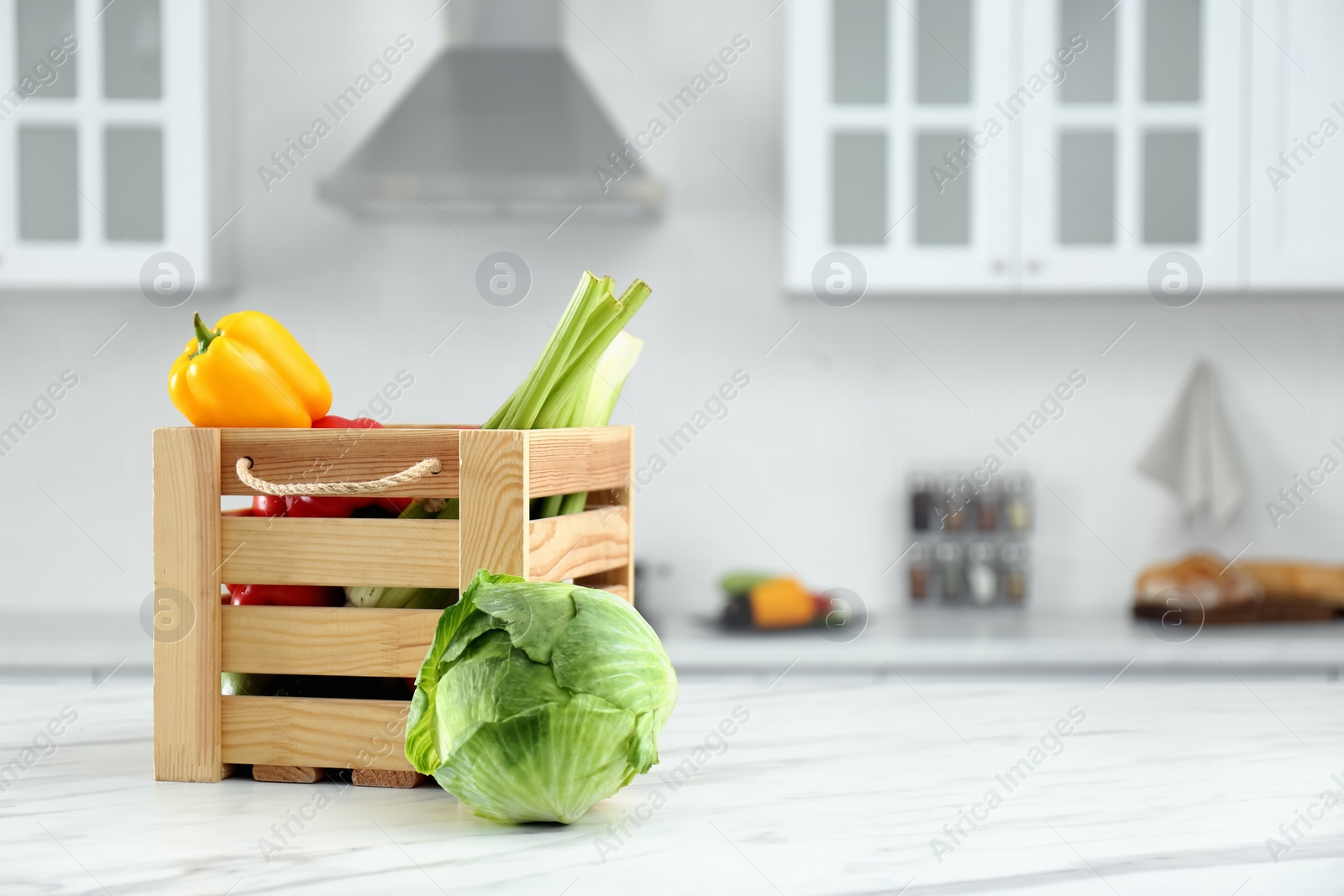 Photo of Different fresh vegetables in wooden crate on white kitchen table. Space for text