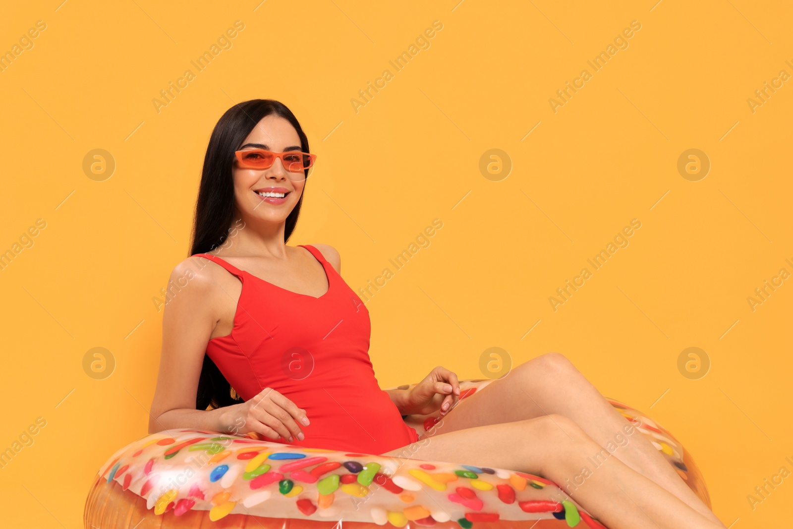 Photo of Happy young woman with beautiful suntan and sunglasses on inflatable ring against orange background