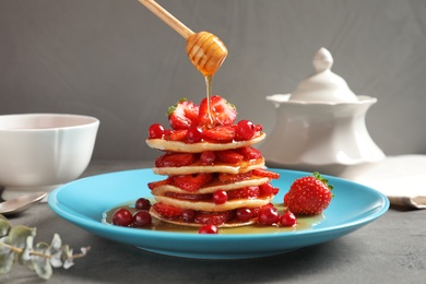 Photo of Pouring honey onto tasty pancakes with berries on plate