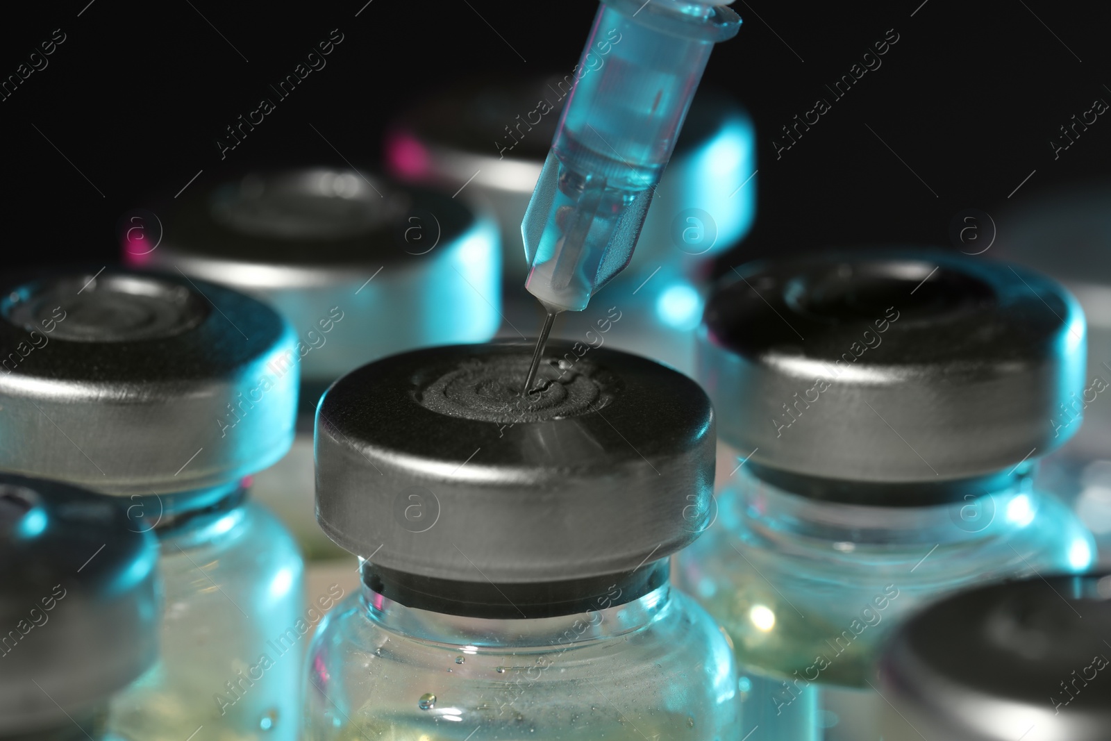 Photo of Filling syringe with medicine from vial against dark background, closeup