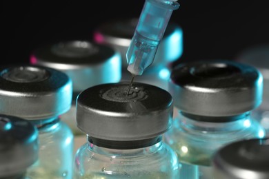 Filling syringe with medicine from vial against dark background, closeup