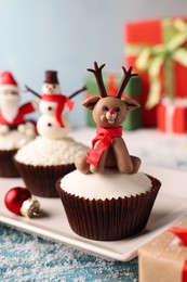 Different beautiful Christmas cupcakes on blue table with snow, closeup