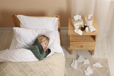 Photo of Sick boy lying in bed near bunch of napkins on floor at home, above view