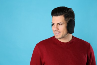 Man wearing stylish earmuffs on light blue background. Space for text