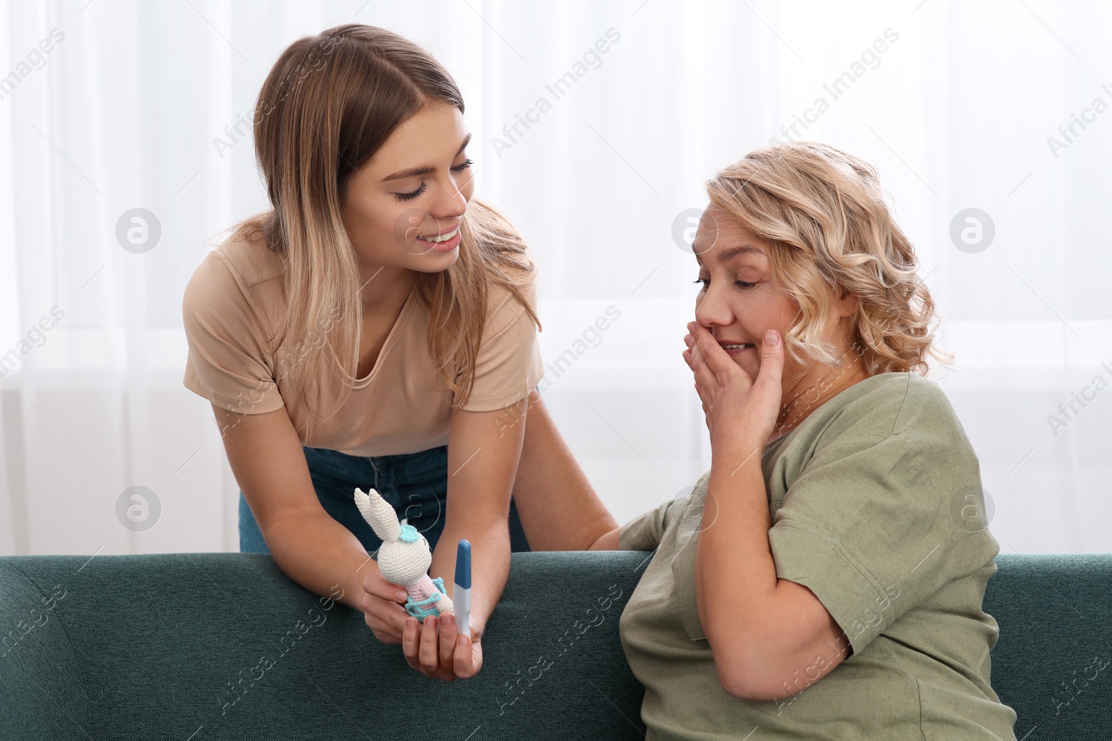 Photo of Young woman with toy bunny showing her mother pregnancy test at home. Grandparent reaction to future grandson