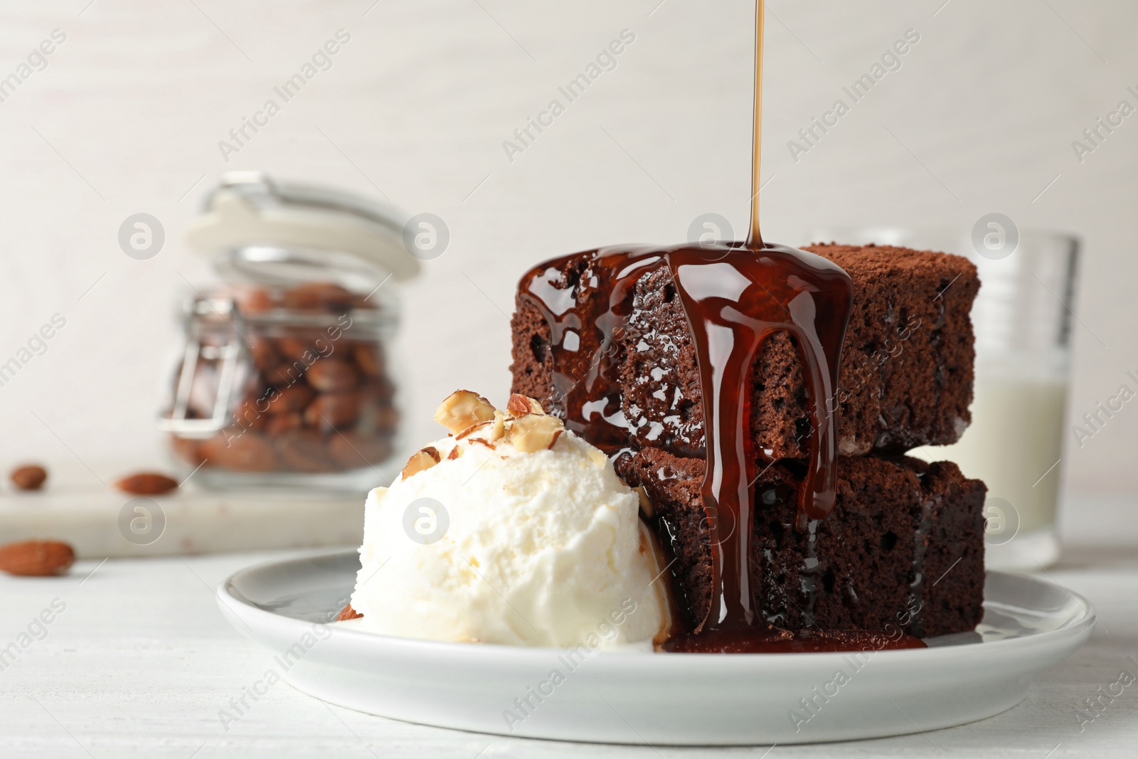 Photo of Pouring sauce onto fresh brownies served with ice-cream on plate, space for text. Delicious chocolate pie